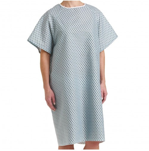 A person wears a loose-fitting, short-sleeved Exam Patient Gown by Calderon Textiles with a blue and white geometric pattern, standing against a plain white background.
